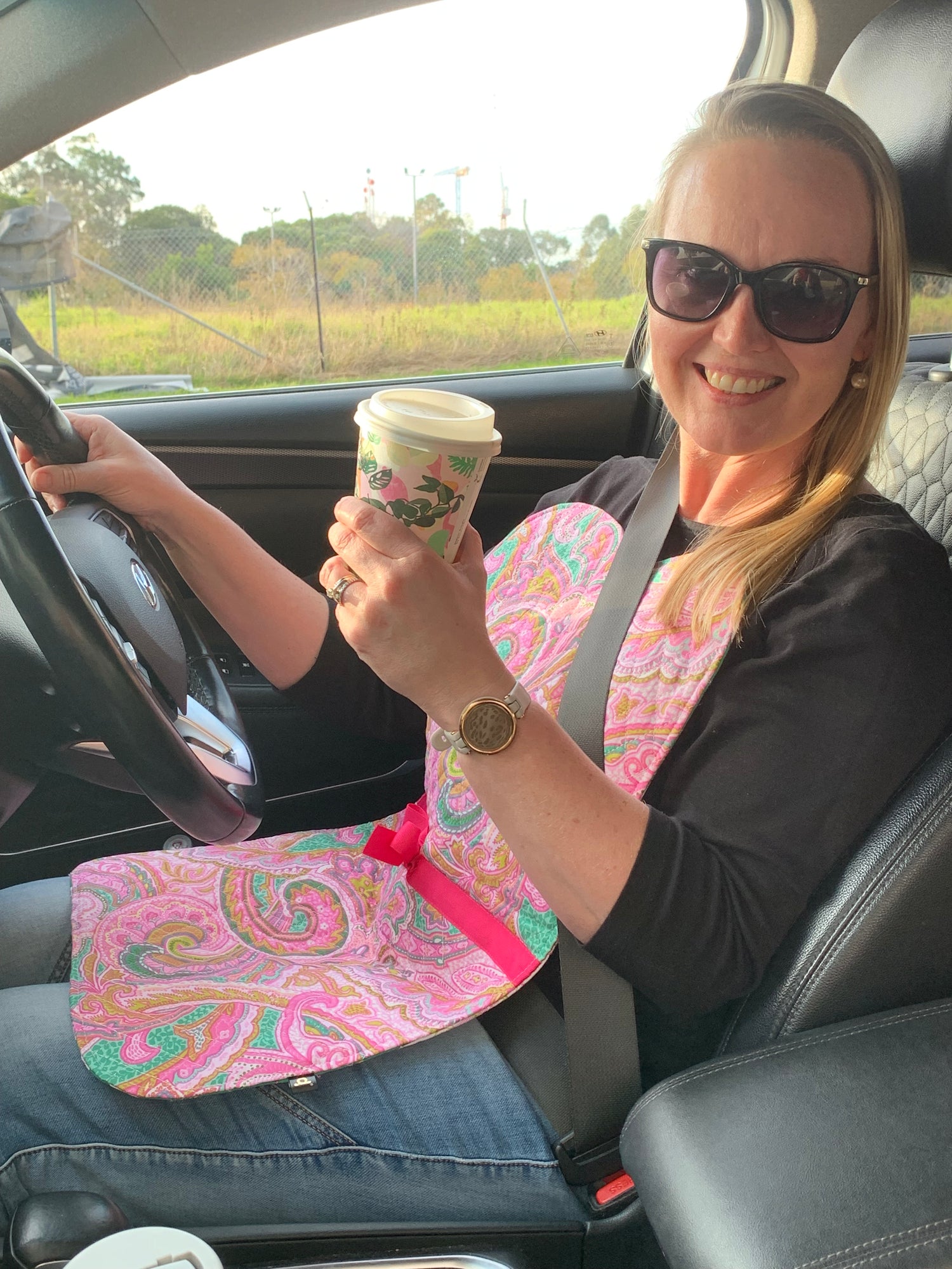 Mother wearing travel napkin drinking coffee on the go in a car while driving